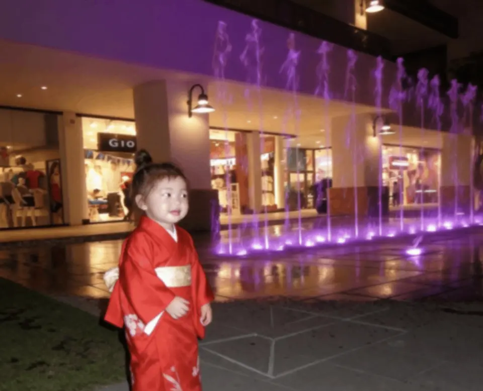 Jemi as a child beside a lit fountain